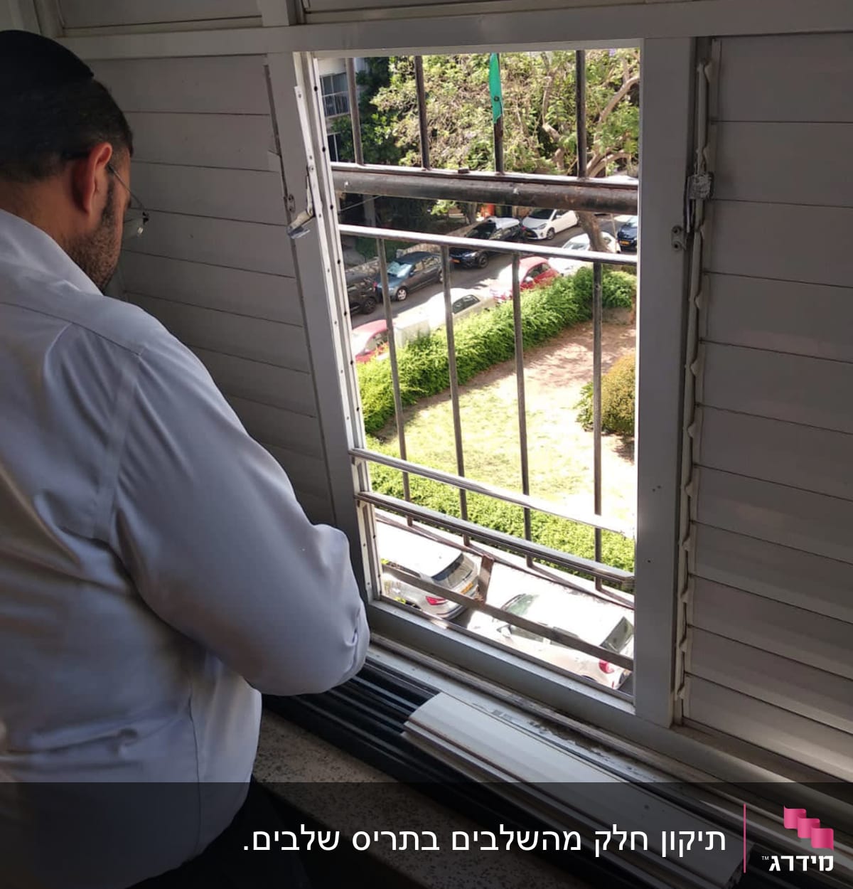 אדם ליד תריסים פתוחים עם חלקי תריס על אדן החלון